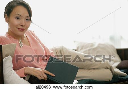 Portrait of a woman lying on sofa, holding a book, looking at camera View Large Photo Image Stock Image - Portrait of a woman lying on sofa, holding a book, looking at camera. Fotosearch