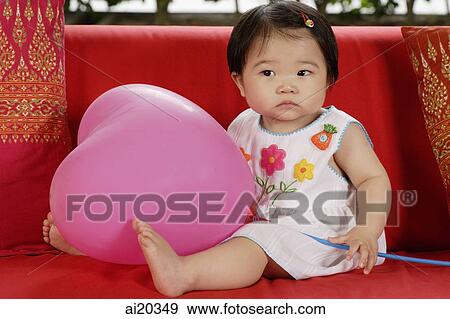 Portrait of baby girl sitting on a red sofa, holding pink balloon View Large Photo Image Stock Photo - Portrait of baby girl sitting on a red sofa, holding pink balloon. Fotosearch