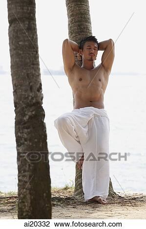 Stock Image - Shirtless man leaning on tree, hands behind head, eyes closed. Fotosearch
