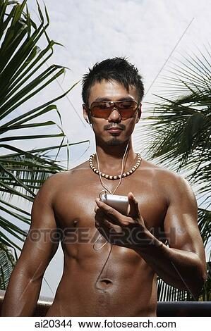 Shirtless man listening to Mp3 player, portrait View Large Photo Image Picture - Shirtless man listening to Mp3 player, portrait. Fotosearch