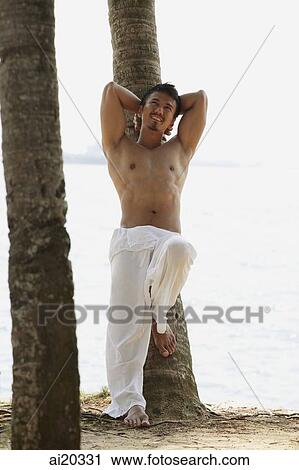 Shirtless man standing on the beach, leaning on tree, hands behind head View Large Photo Image Stock Image - Shirtless man standing on the beach, leaning on tree, hands behind head. Fotosearch