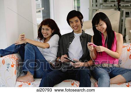 Teenagers sitting side by side, on sofa, listening to music from MP3 players View Large Photo Image Stock Image - Teenagers sitting side by side, on sofa, listening to music from MP3 players. Fotosearch