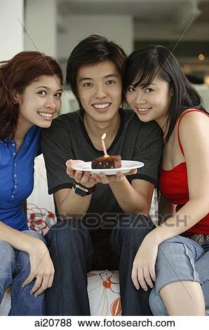 Teenagers sitting side by side, smiling at camera, boy in the middle holding plate with a cake and candle on it View Large Photo Image Stock Photo - Teenagers sitting side by side, smiling at camera, boy in the middle holding plate with a cake and candle on it. Fotosearch