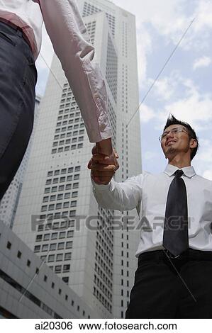 Two businessmen shaking hands, city location View Large Photo Image Stock Photograph - Two businessmen shaking hands, city location. Fotosearch