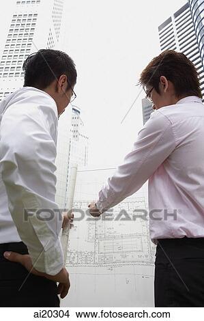 Two men looking at blueprint, buildings in the background View Large Photo Image Picture - Two men looking at blueprint, buildings in the background. Fotosearch