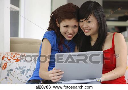 Stock Image - Two teenage girls sitting side by side looking at laptop. Fotosearch