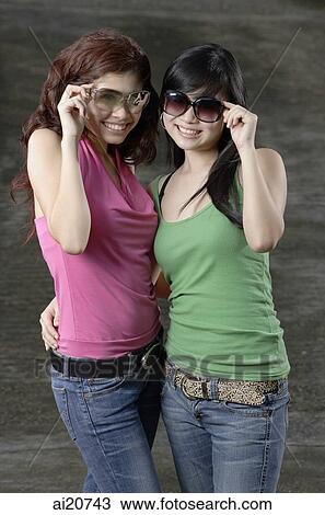 Two teenage girls, standing side by side, adjusting sunglasses View Large Photo Image Stock Image - Two teenage girls, standing side by side, adjusting sunglasses. Fotosearch