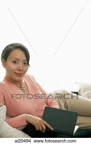 Woman lying on sofa, holding a book, looking at camera View Large Photo Image Picture - Woman lying on sofa, holding a book, looking at camera. Fotosearch