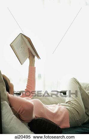 Woman lying on sofa, reading a book, arm outstretched View Large Photo Image Stock Photography - Woman lying on sofa, reading a book, arm outstretched. Fotosearch