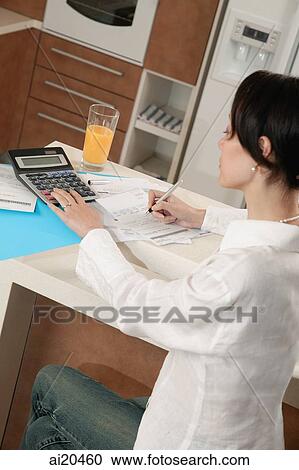 Stock Image - Woman sitting at kitchen counter with calculator and bills. Fotosearch