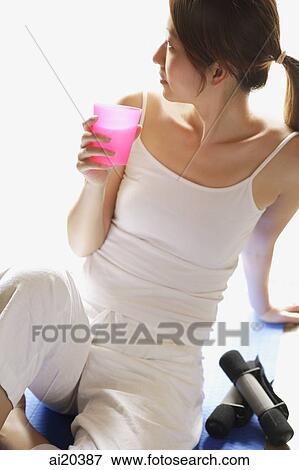 Stock Photo - Woman sitting on floor, holding glass, looking away. Fotosearch