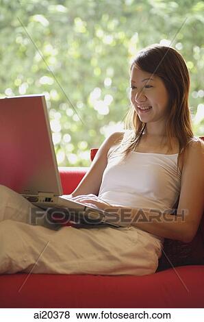 Woman sitting on sofa, using laptop View Large Photo Image Stock Photo - Woman sitting on sofa, using laptop. Fotosearch