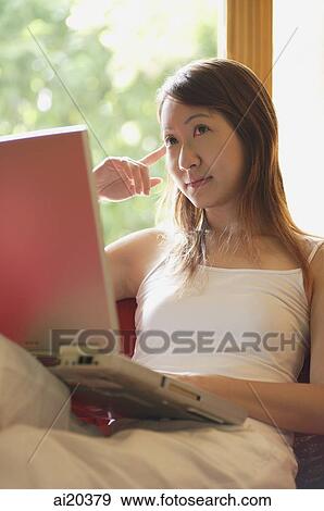 Woman sitting on sofa with laptop, looking away View Large Photo Image Stock Photo - Woman sitting on sofa with laptop, looking away. Fotosearch