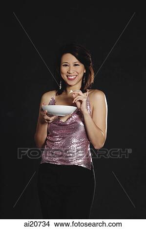 Picture - Woman standing against black background, holding bowl. Fotosearch