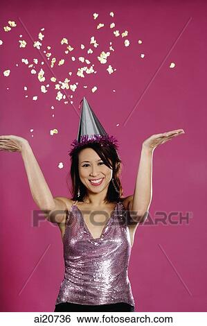 Stock Photograph - Woman wearing party hat, throwing popcorn in air. Fotosearch