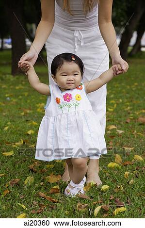Young girl walking, mother standing behind her, holding her hands View Large Photo Image Stock Image - Young girl walking, mother standing behind her, holding her hands. Fotosearch
