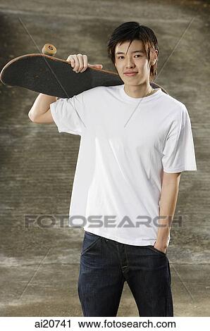 Young man holding skateboard over shoulder View Large Photo Image Stock Image - Young man holding skateboard over shoulder. Fotosearch