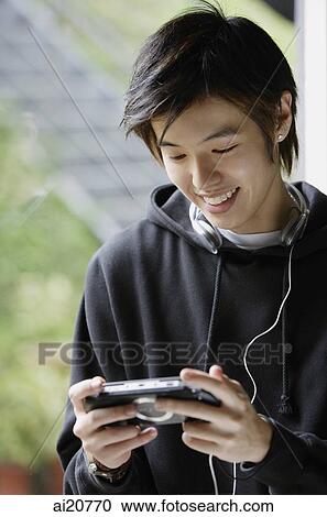 Young man looking at MP3 player, smiling View Large Photo Image Stock Image - Young man looking at MP3 player, smiling. Fotosearch