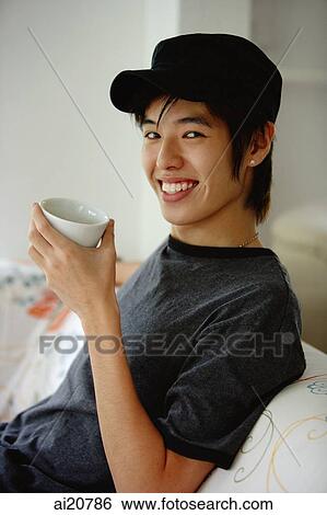 Young man sitting on sofa, holding cup View Large Photo Image Stock Photograph - Young man sitting on sofa, holding cup. Fotosearch