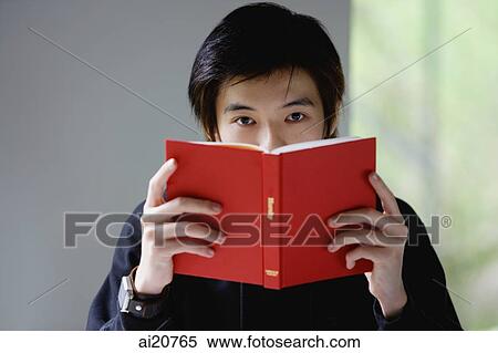 Young man with book covering his face, looking at camera View Large Photo Image Stock Photography - Young man with book covering his face, looking at camera. Fotosearch