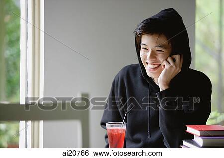 Young man with hooded jacket, drink in front of him, smiling View Large Photo Image Stock Photograph - Young man with hooded jacket, drink in front of him, smiling. Fotosearch