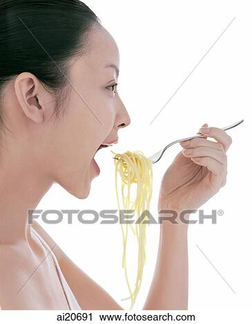 Stock Image - Young woman eating spaghetti, side view. Fotosearch