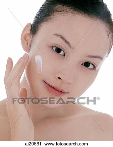 Young woman looking at camera, applying moisturizer on face View Large Photo Image Stock Image - Young woman looking at camera, applying moisturizer on face. Fotosearch
