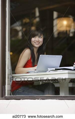 Young woman sitting at table, using laptop, looking through window View Large Photo Image Stock Image - Young woman sitting at table, using laptop, looking through window. Fotosearch