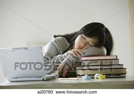 Stock Image - Young woman sleeping on stack of books, laptop open next to her. Fotosearch