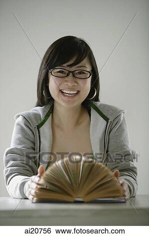 Stock Photograph - Young woman smiling at camera, open book in front of her. Fotosearch