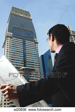 Businessman holding blueprint, looking at building View Large Photo Image Stock Photograph - Businessman holding blueprint, looking at building. Fotosearch