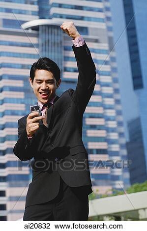 Stock Image - Businessman looking at mobile phone, hand raised in a fist. Fotosearch