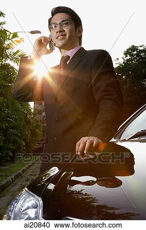 Businessman standing next to car, holding mobile phone View Large Photo Image Stock Image - Businessman standing next to car, holding mobile phone. Fotosearch