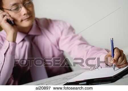 Businessman using mobile phone, writing on notepad View Large Photo Image Stock Photo - Businessman using mobile phone, writing on notepad. Fotosearch