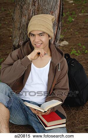 College student sitting at base of tree, holding notebook, looking at camera View Large Photo Image Stock Photography - College student sitting at base of tree, holding notebook, looking at camera. Fotosearch