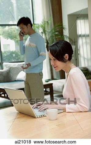 Couple at home, woman using laptop, man in the background on the phone View Large Photo Image Stock Photo - Couple at home, woman using laptop, man in the background on the phone. Fotosearch