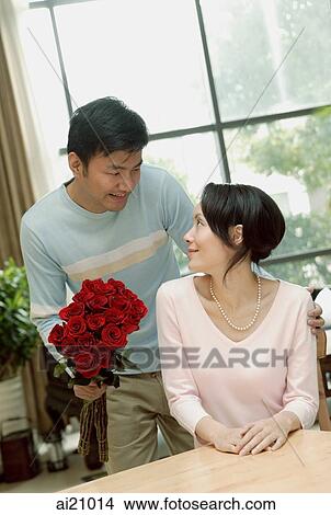 Couple in loving room, man holding bouquet of flowers, woman turning to look at him View Large Photo Image Picture - Couple in loving room, man holding bouquet of flowers, woman turning to look at him. Fotosearch