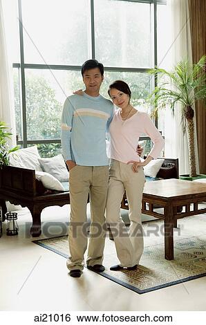 Stock Photograph - Couple standing in living room, looking at camera. Fotosearch