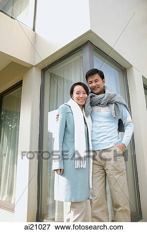 Stock Photo - Couple standing outside house, smiling at camera. Fotosearch