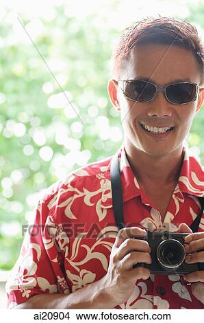 Man in floral shirt and sunglasses holding a camera View Large Photo Image Picture - Man in floral shirt and sunglasses holding a camera. Fotosearch