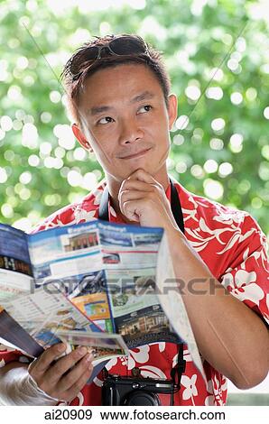 Stock Photo - Man in floral shirt holding a map, hand on chin. Fotosearch