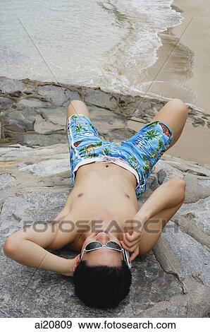 Man lying on rocks at beach, using mobile phone View Large Photo Image Stock Photo - Man lying on rocks at beach, using mobile phone. Fotosearch