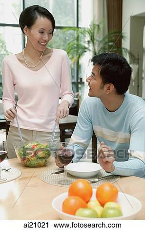 Man sitting at dining table, woman standing next to him tossing a salad View Large Photo Image Stock Image - Man sitting at dining table, woman standing next to him tossing a salad. Fotosearch