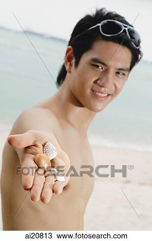 Man standing on beach, holding shells and stones in palm of hand View Large Photo Image Stock Image - Man standing on beach, holding shells and stones in palm of hand. Fotosearch