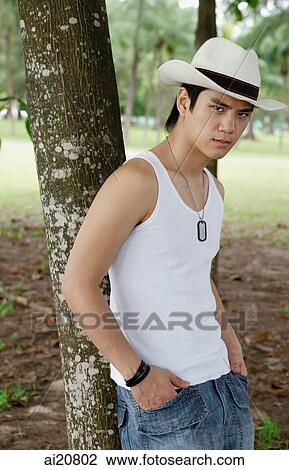 Man wearing hat, leaning on tree, hand in pocket View Large Photo Image Stock Image - Man wearing hat, leaning on tree, hand in pocket. Fotosearch