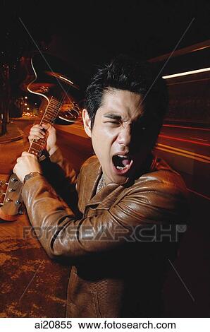 Stock Photography - Young man holding guitar, making face. Fotosearch