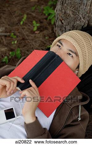 Stock Image - Young man listening to MP3 player, face obscured by book. Fotosearch