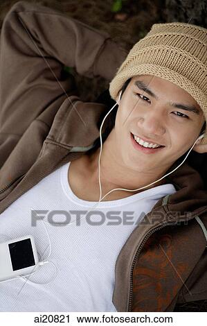 Young man listening to MP3 player, smiling at camera View Large Photo Image Stock Image - Young man listening to MP3 player, smiling at camera. Fotosearch