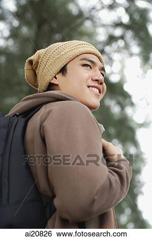 Stock Photograph - Young man with cap and backpack, smiling, looking away. Fotosearch