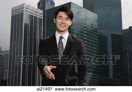 Businessman holding hand out toward camera, buildings in the background View Large Photo Image Stock Photo - Businessman holding hand out toward camera, buildings in the background. Fotosearch